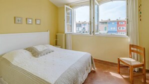 Ein Schlafzimmer mit einem Bett, einem Sessel und einem Fenster mit Blick auf farbenfrohe Gebäude.
