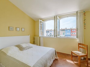 Ein Schlafzimmer mit einem Bett, einem Sessel und einem Fenster mit Blick auf farbenfrohe Gebäude.