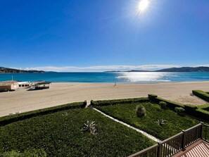 A beach view with a clear sky, a sandy beach, and a well-maintained garden area with a wooden deck. - 3-bedroom apartment with sea view, beach access, parking, in Port Grimaud (Port Grimaud)