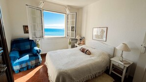 A bedroom with a bed, a chair, a nightstand, a lamp, a window with curtains, and a view of the sea. - 3-bedroom apartment with sea view, beach access, parking, in Port Grimaud (Port Grimaud)