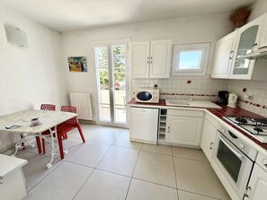 A compact kitchen with white cabinets, a microwave, a stove, and a dining area with a table and chairs. - Charming Duplex in Port Grimaud with Balconies and Parking (Port Grimaud)
