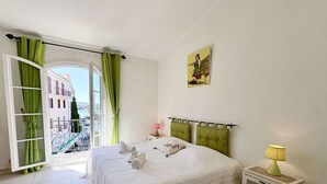 Ein Schlafzimmer mit einem Bett, einem Nachttisch, einer Lampe, einem Fenster mit Vorhängen und einem Bild an der Wand.