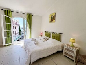 A bedroom with a bed, a nightstand, a lamp, a window with curtains, and a painting on the wall. - Charming Duplex in Port Grimaud with Balconies and Parking (Port Grimaud)