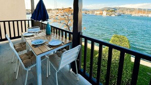 Un balcon avec une table dressée pour le dîner, donnant sur une étendue d’eau où l’on aperçoit des bateaux et des bâtiments au loin.