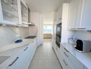 A modern kitchen with white cabinets, a marble countertop, and a view to a balcony. - Spacious apartment with balcony and beach access in Port Grimaud (Port Grimaud)