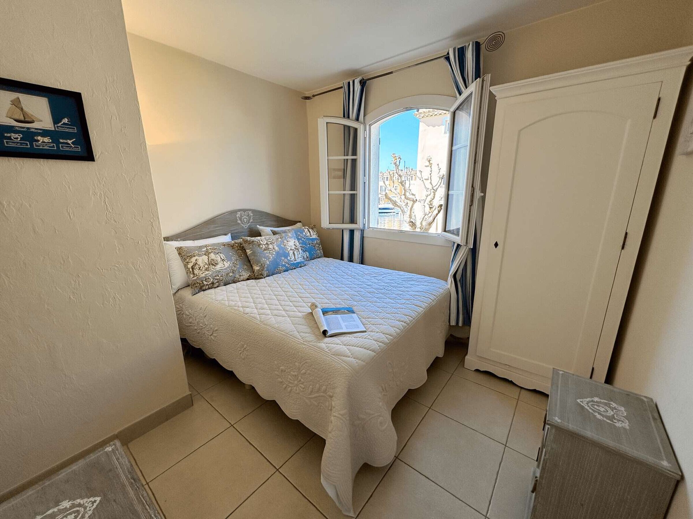 A bedroom with a bed, a window with curtains, a door, and a framed picture on the wall.