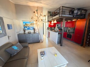 A compact living space with a sofa, a coffee table, a kitchen with red cabinets, and a loft area with storage. - Renovated apartment with Internet, 2 bedrooms, parking in Port Grimaud (Port Grimaud)