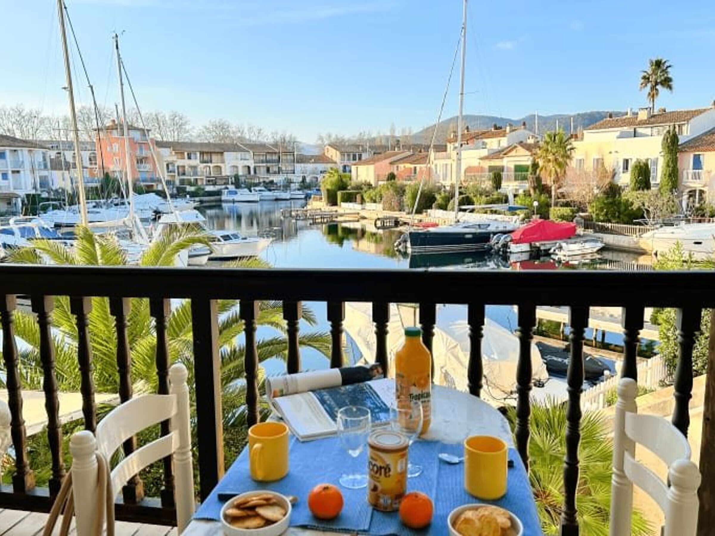 A balcony with a table set for breakfast, overlooking a marina with boats and houses.