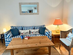 Ein Wohnzimmer mit einem gestreiften Sofa, einem Holztisch, einem Korbstuhl, einer Lampe und einem Spiegel an der Wand.