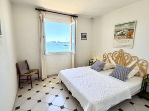 A bedroom with a bed, a chair, a window with a view of the sea, and a painting on the wall. - 4-room apartment with balcony, sea view, wifi and parking (Port Grimaud)
