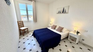Ein Schlafzimmer mit Bett, Sessel, Nachttisch, Lampe und einem Bild an der Wand.
