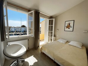 Ein Schlafzimmer mit Bett, Fenster, Heizkörper und einem Badezimmer mit Waschbecken.