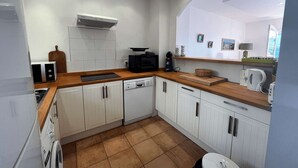 Een kleine keuken met witte kastjes, een houten aanrecht, een ingebouwde magnetron en een vaatwasser.