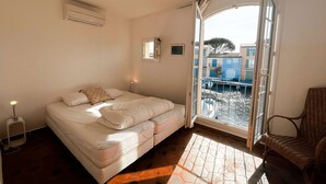 Een slaapkamer met een bed, een stoel, een raam en uitzicht op gebouwen.