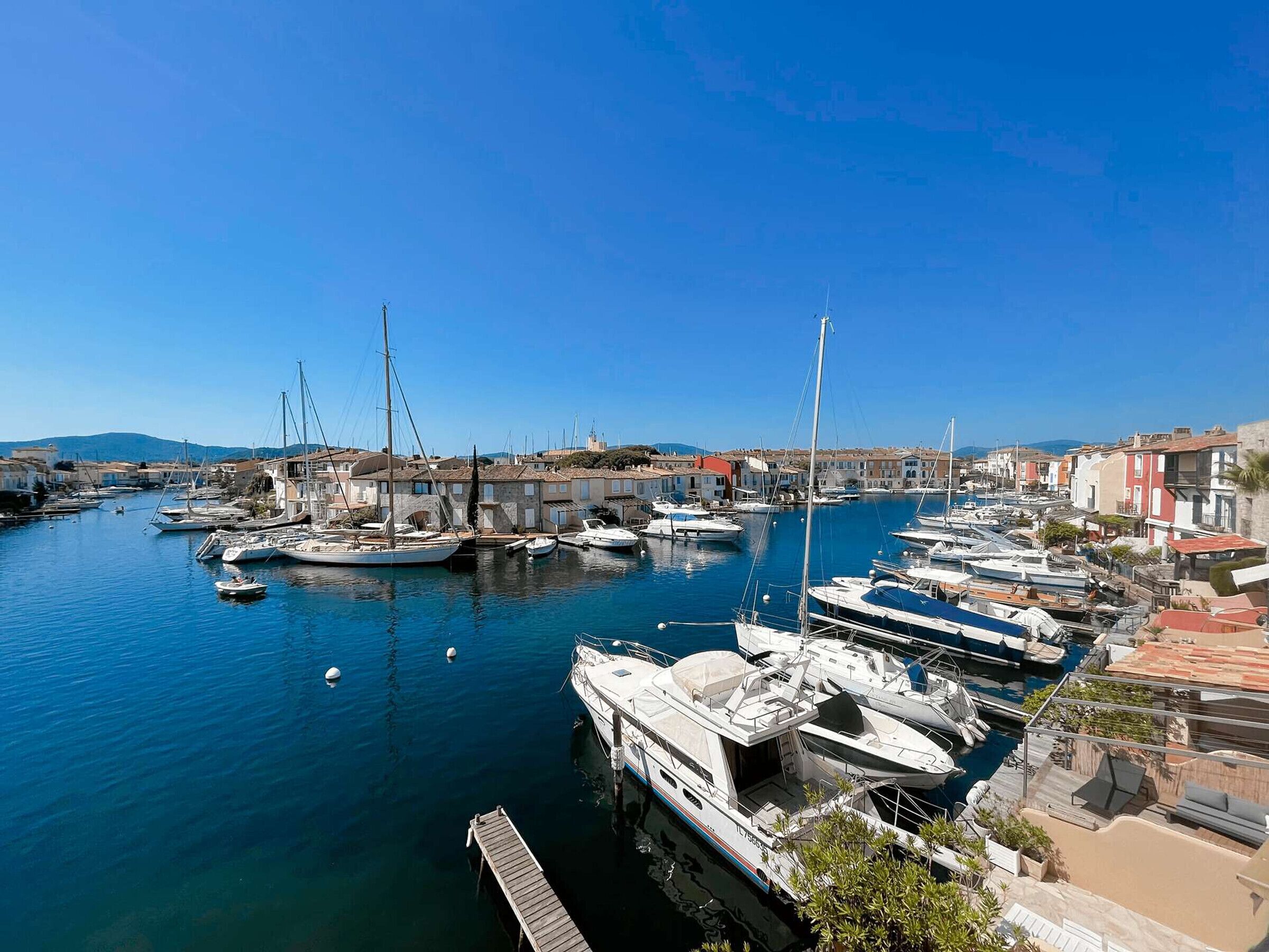 A marina with boats docked, a clear blue sky, and buildings in the background.