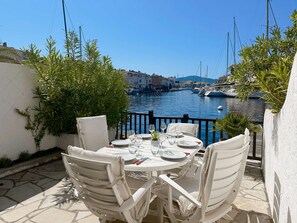 A table set for dining with chairs, overlooking a marina with boats and buildings. - Renovated House in Port Grimaud - AC - WIFI - Parking - Mooring (Port Grimaud)
