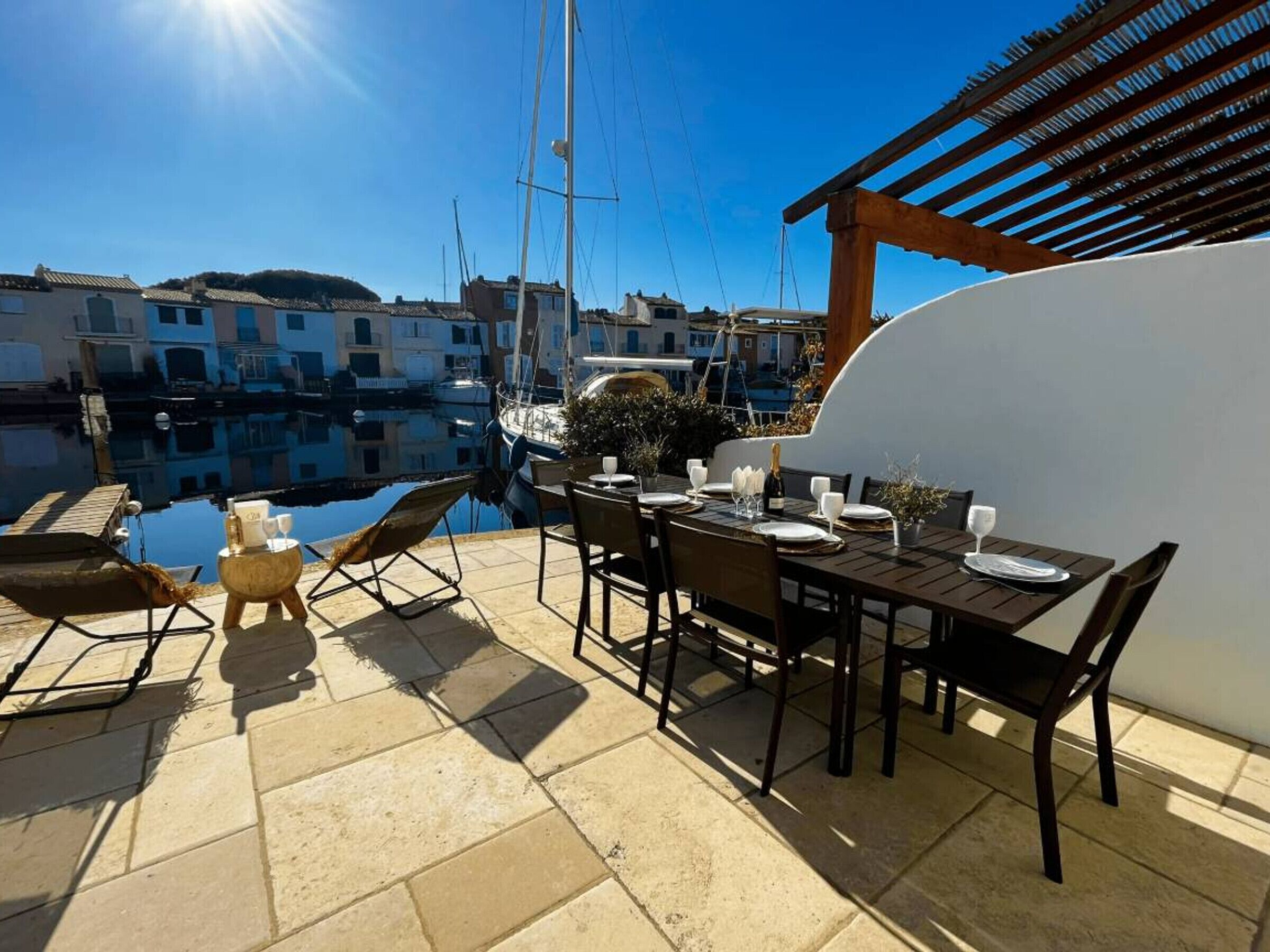 A terrace with a table set for dining, overlooking a marina with boats and buildings.