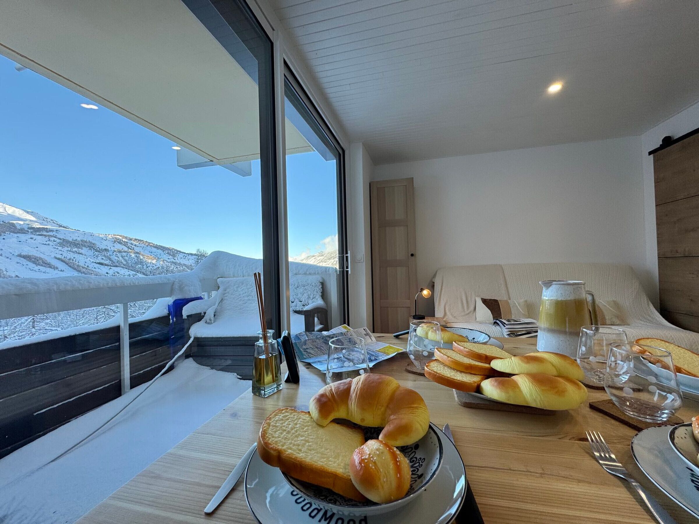A breakfast table with bread, a pitcher, and glasses, overlooking a snowy landscape.