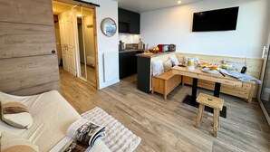 A modern kitchen with a dining area, wooden flooring, and a TV mounted on the wall. - Vars - Cozy Apartment for 4 People (Vars)