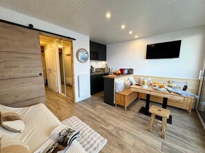 A modern kitchen with a dining area, wooden flooring, and a TV mounted on the wall. - Vars - Cozy Apartment for 4 People (Vars)
