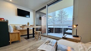 A modern living room with a large window, a flat-screen TV, a wooden table, and a magazine on the floor. - Vars - Cozy Apartment for 4 People (Vars)