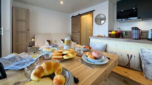 A cozy living room with a wooden dining table set for breakfast, a sofa, and a kitchen area with modern appliances. - Vars - Cozy Apartment for 4 People (Vars)