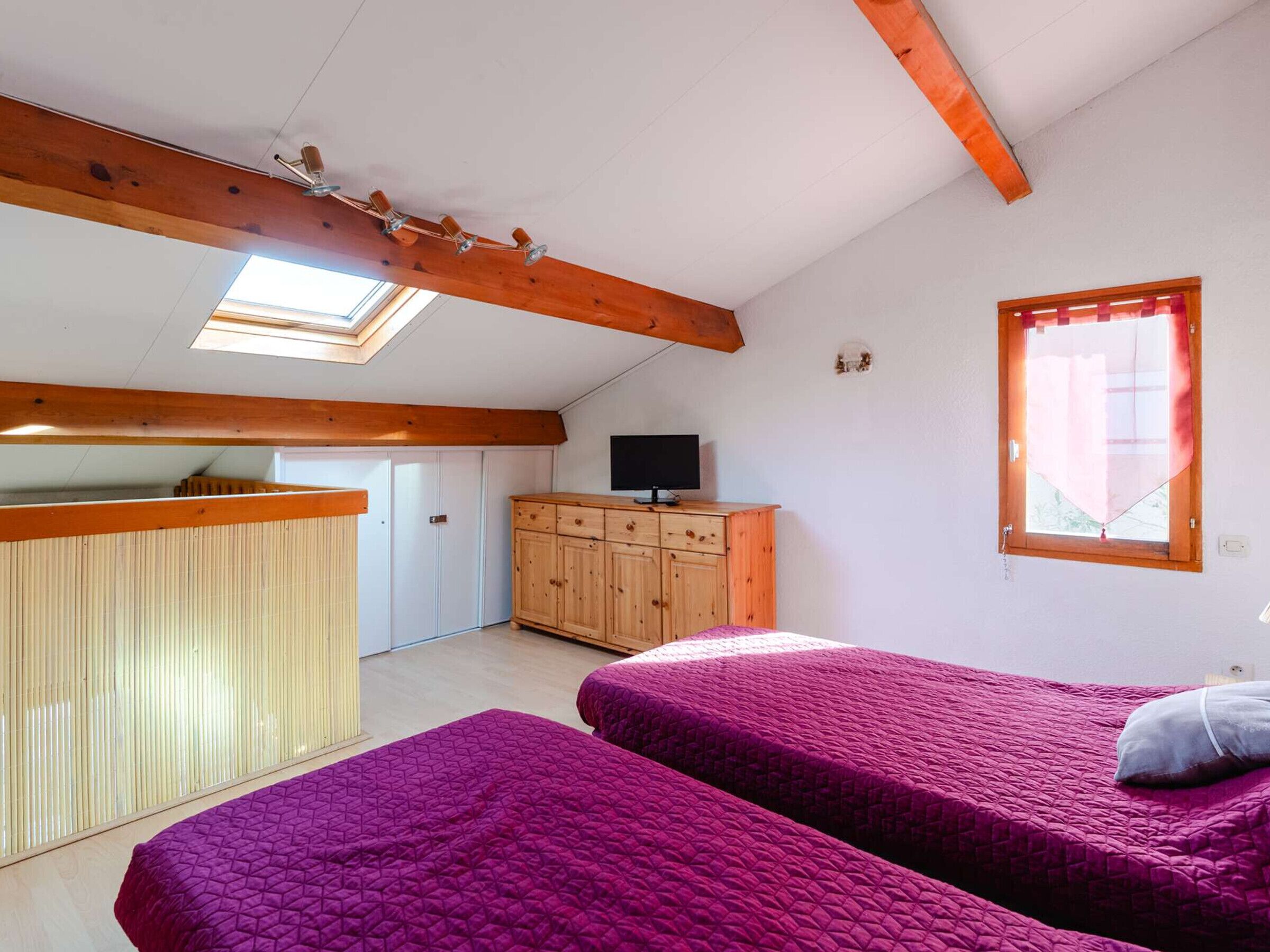Une chambre avec deux lits, une armoire en bois, un téléviseur et une lucarne.