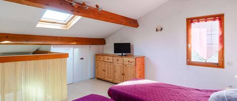 Une chambre avec deux lits, une armoire en bois, un téléviseur et une lucarne.