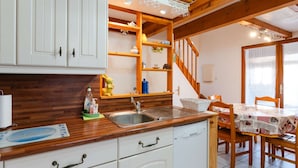 Una cocina con armarios blancos, encimera de madera y un fregadero. Hay una mesa de comedor con sillas y una ventana con persianas.