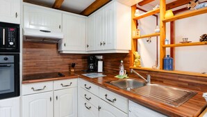 Una cocina con armarios blancos, encimeras de madera, horno empotrado, cafetera y una estantería con diversos utensilios de cocina.