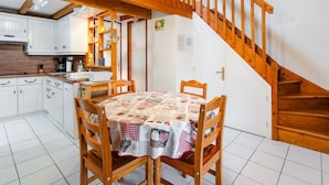 Una cocina acogedora con vigas de madera, una mesa de comedor con mantel a cuadros y una escalera de madera.