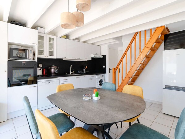 A modern kitchen with white cabinets, a dining table with colorful chairs, a microwave, a stove, and a wooden staircase.