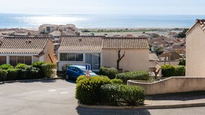 A residential area with terracotta-tiled houses, a parked car, and a view of the sea. - 3-room Pavilion with sea view, pool and terrace, pets welcome (Fleury-Saint-Pierre-la-Mer)