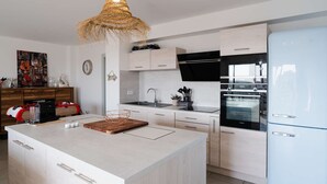 Eine moderne Küche mit einer zentralen Kochinsel, weißen Schränken, einem eingebauten Backofen und einem weißen Kühlschrank.