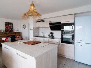 A modern kitchen with a central island, white cabinetry, a built-in oven, and a white refrigerator. - Bright, air-conditioned apartment with WIFI and parking in Narbonne-Plage (Narbonne-Narbonne Plage-Narbonne Plage)