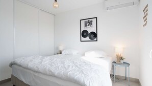 Ein modernes Schlafzimmer mit einem großen Bett, Nachttischlampen, einem gerahmten Bild und einer Klimaanlage.
