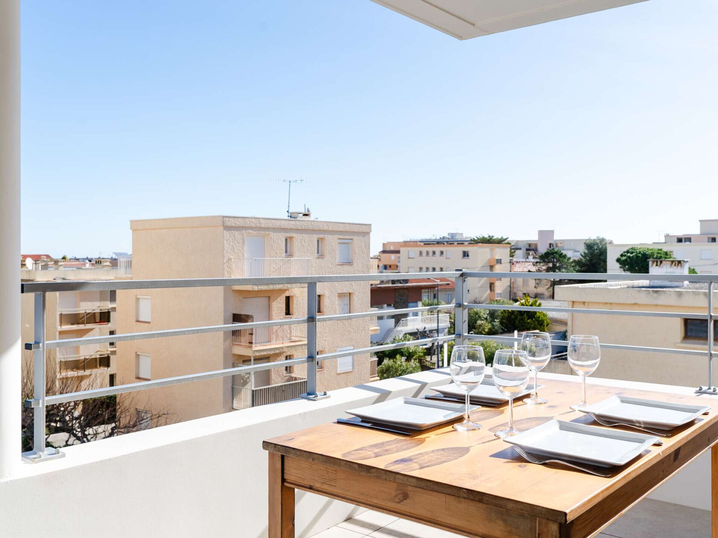 A balcony with a wooden table set for dining, overlooking a residential area.
