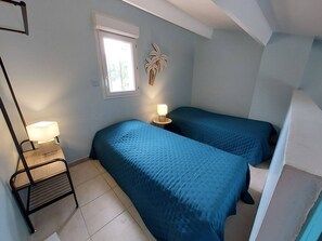 A bedroom with two beds, a nightstand, a lamp, a window, and a wall-mounted plant. - Air-conditioned pavilion for 6 pers. with parking & bikes in Gruissan (Gruissan)