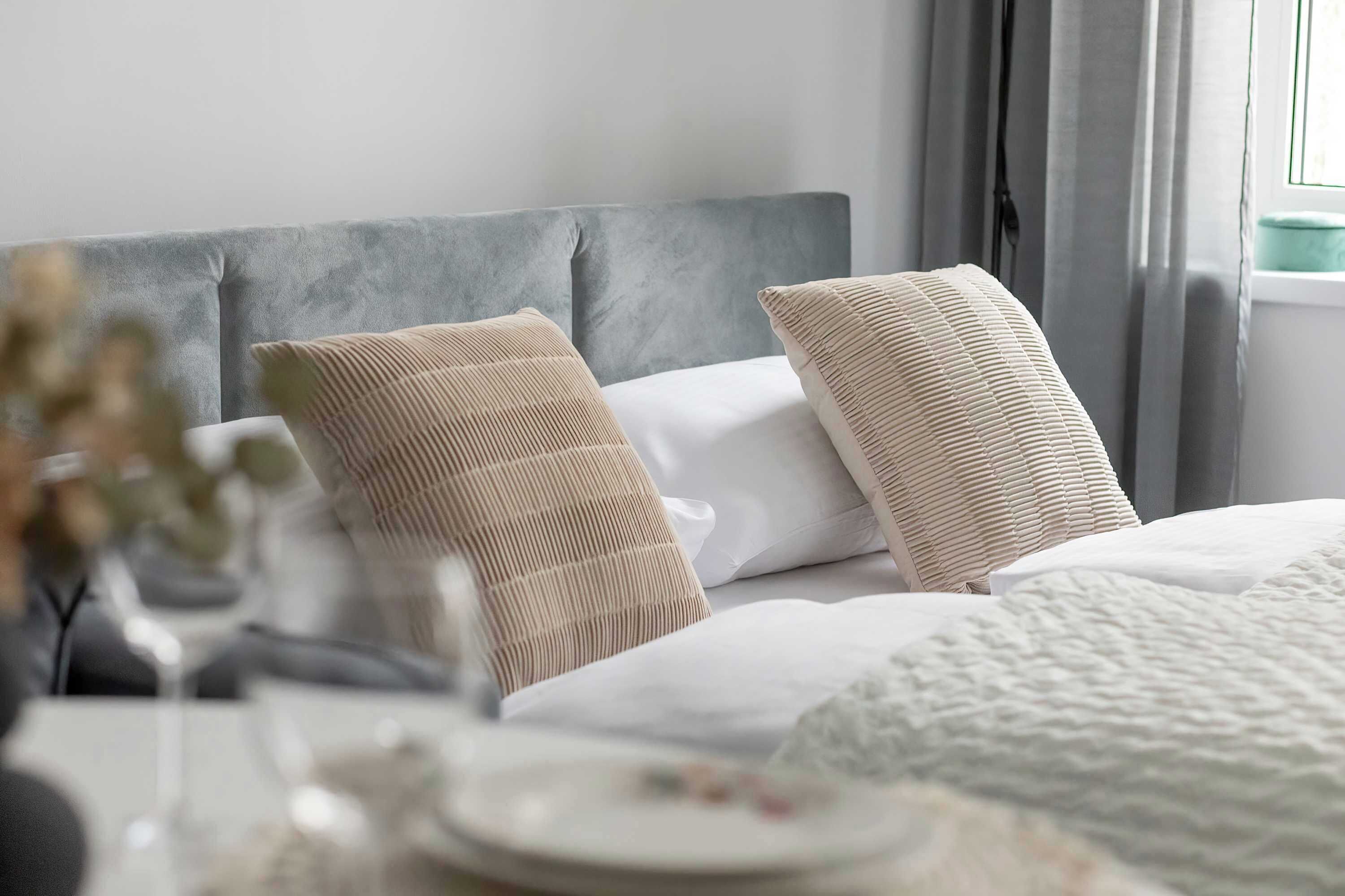 Una cama bien hecha con cabecera gris, ropa de cama blanca y almohadas beige.