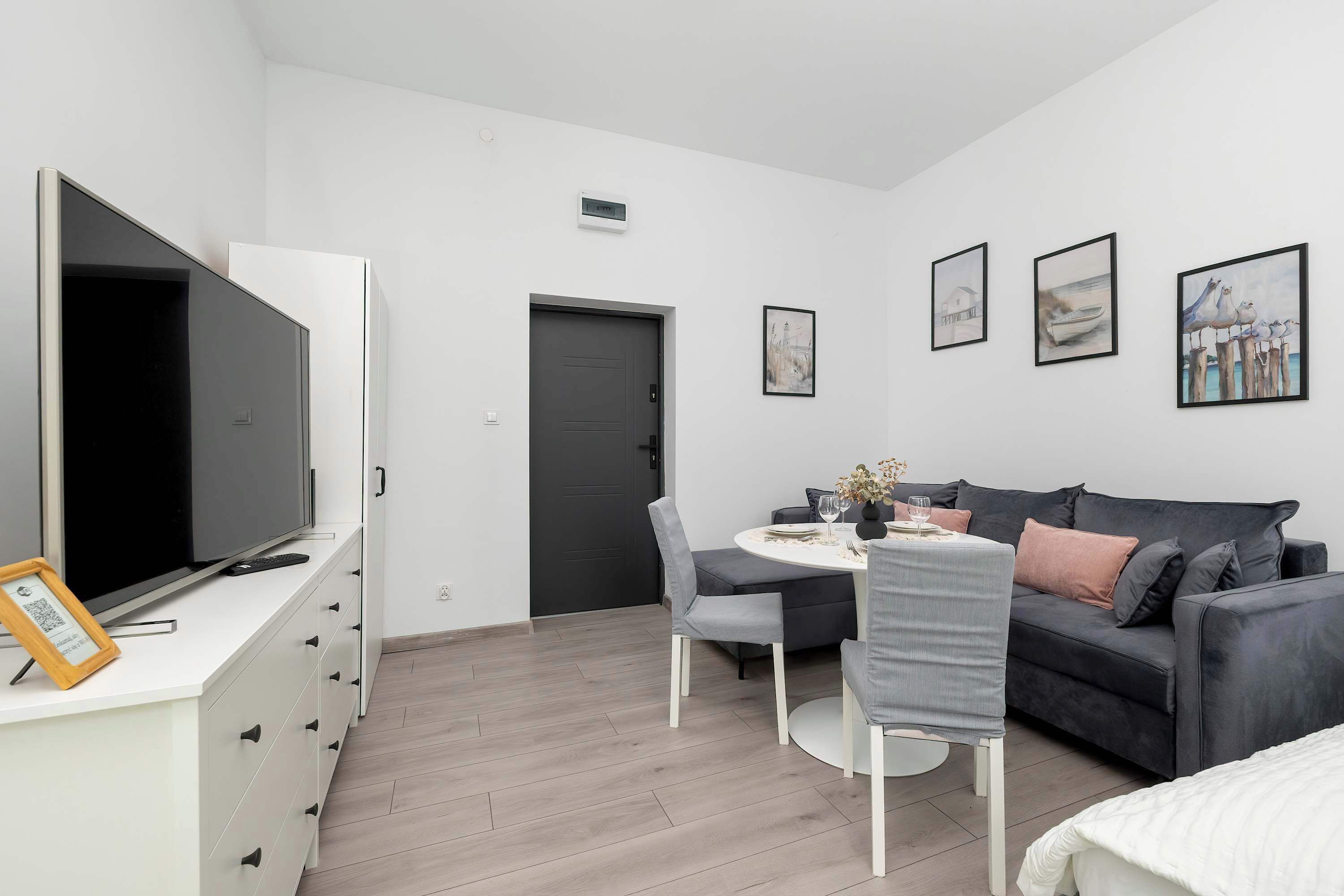 Ein modernes Wohnzimmer mit Flachbildfernseher, grauem Sofa, Esstisch und einem Kunstwerk an der Wand.