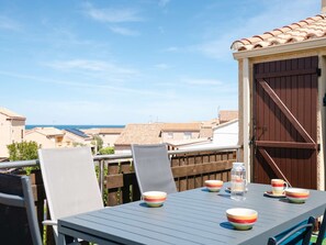 A balcony with a table set for dining, overlooking a residential area and the sea.