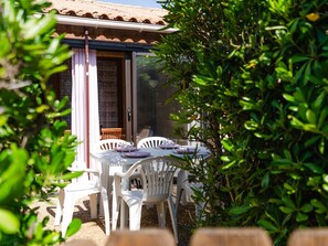 Un espace extérieur aménagé pour les repas, avec des chaises et des tables en plastique blanc, une porte en bois et un toit recouvert de tuiles.