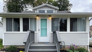 A single-story house with a front porch, a set of stairs leading to the door, and a small garden with yellow flowers. - Cozy Cottage 2BR Queen Families Workers Nurses (Chippewa Lake)