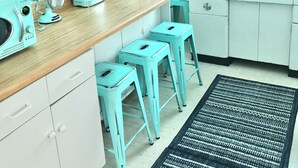 A kitchen with a wooden countertop, a coffee maker, a toaster, and a sink. There are three blue stools and a black and white rug on the floor. - Cozy Cottage 2BR Queen Families Workers Nurses (Chippewa Lake)