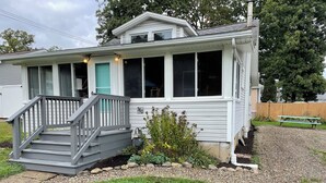 A single-story house with a front porch, a small garden, and a gravel driveway. - Cozy Cottage 2BR Queen Families Workers Nurses (Chippewa Lake)