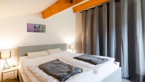 Una cama bien hecha con dos mantas dobladas, una lámpara de noche y un cuadro en la pared.