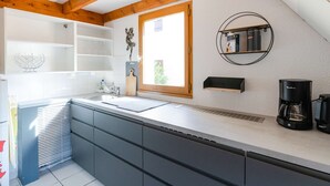 Una cocina moderna con vigas de madera, armarios blancos, horno empotrado y cafetera.