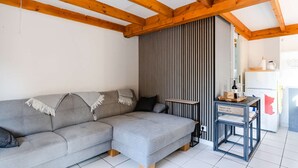 Una sala de estar moderna con un sofá seccional gris, vigas de madera, una pared a rayas y una pequeña mesa con una botella y vasos.