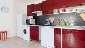 Een kleine keuken met rode kastjes, een magnetron, een koffiezetapparaat en een wasmachine.