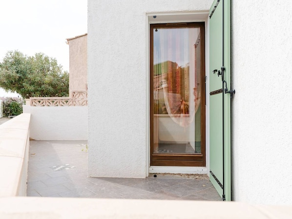 A modern building entrance with a glass door, a small step leading up to it, and a white wall. - Charming Villa in Gruissan - 2 Bedrooms, 6 Guests, Near Beach, WiFi & Garage (Gruissan)